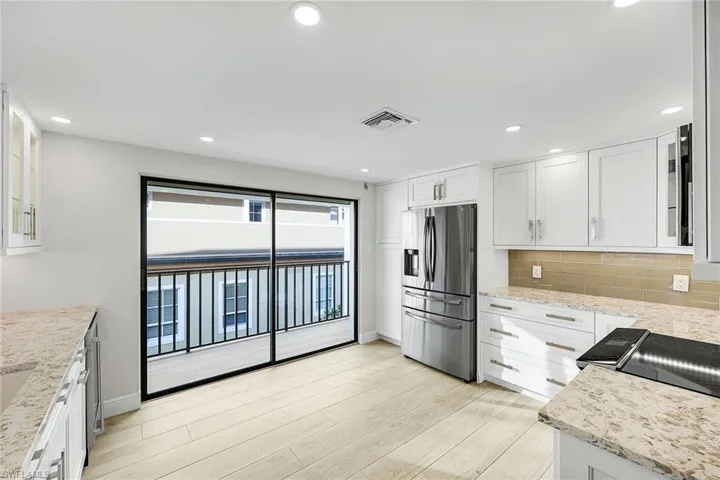 Kitchen featuring glass insert cabinets, light stone counters, stainless steel refrigerator with ice dispenser, white cabinets, and recessed lighting