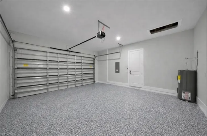 Garage with water heater, electric panel, and a garage door opener