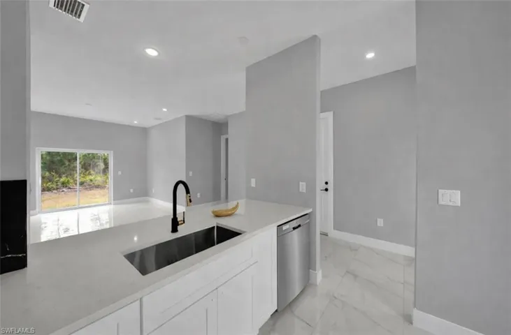 Kitchen with white cabinets, stainless steel dishwasher, light stone countertops, recessed lighting, and light marble finish floors