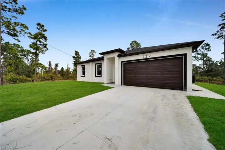 Prairie-style home featuring concrete driveway, a front lawn, stucco siding, and an attached garage
