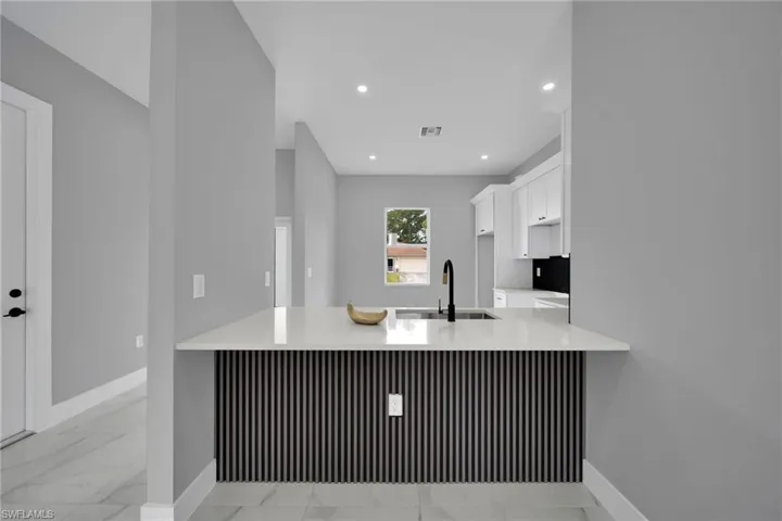 Kitchen with white cabinetry, a peninsula, light marble finish floors, light stone countertops, and recessed lighting