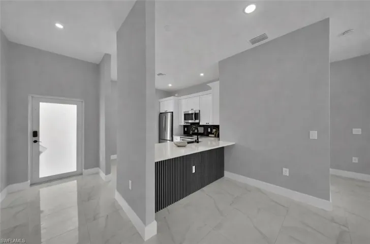 Kitchen with a peninsula, white cabinetry, appliances with stainless steel finishes, light marble finish flooring, and recessed lighting