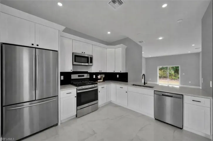 Kitchen featuring appliances with stainless steel finishes, white cabinetry, light marble finish flooring, recessed lighting, and light stone counters