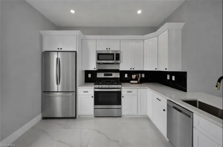 Kitchen featuring appliances with stainless steel finishes, white cabinets, backsplash, and light marble finish flooring