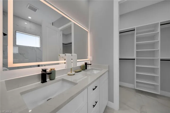 Bathroom with a walk in closet, light marble finish flooring, double vanity, a marble finish shower, and recessed lighting