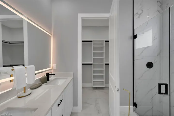 Bathroom featuring a walk in closet, double vanity, a marble finish shower, and light marble finish flooring