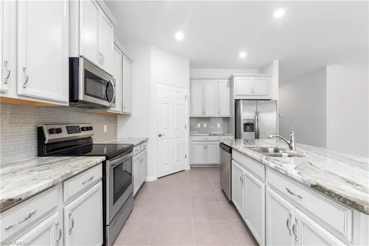 Kitchen featuring stainless steel appliances, sink, backsplash, light stone countertops, and light tile patterned flooring