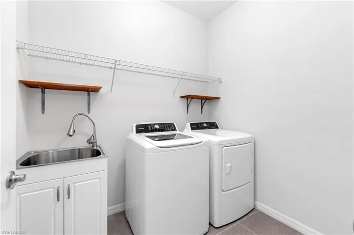 Laundry room with cabinets, light tile patterned floors, washer and clothes dryer, and sink