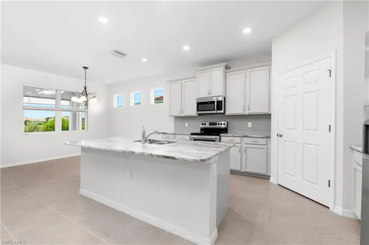 Kitchen with decorative light fixtures, white cabinetry, an island with sink, appliances with stainless steel finishes, and light tile patterned floors