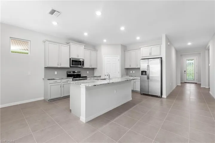 Kitchen featuring stainless steel appliances, sink, light stone counters, a kitchen island with sink, and white cabinetry