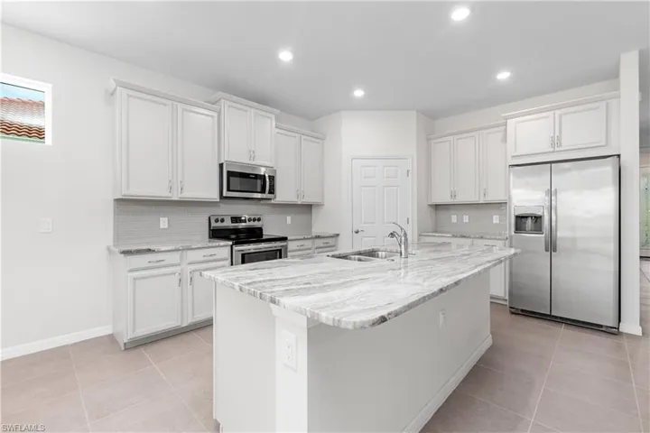 Kitchen with light tile patterned floors, backsplash, an island with sink, appliances with stainless steel finishes, and sink