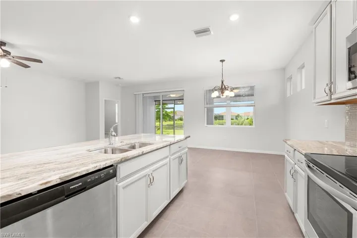 Kitchen featuring stainless steel appliances, ceiling fan with notable chandelier, white cabinets, sink, and light tile patterned floors