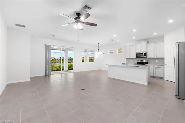 Kitchen featuring stainless steel appliances, hanging light fixtures, light tile patterned floors, a kitchen island with sink, and ceiling fan
