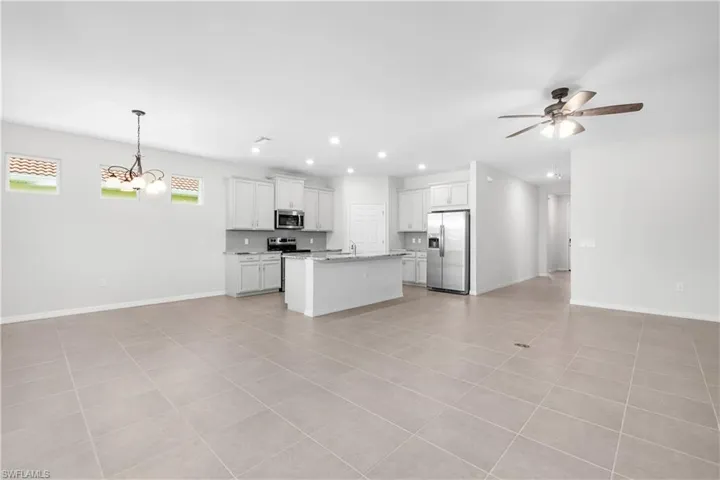 Kitchen with stainless steel appliances, ceiling fan with notable chandelier, pendant lighting, a center island with sink, and light tile patterned floors