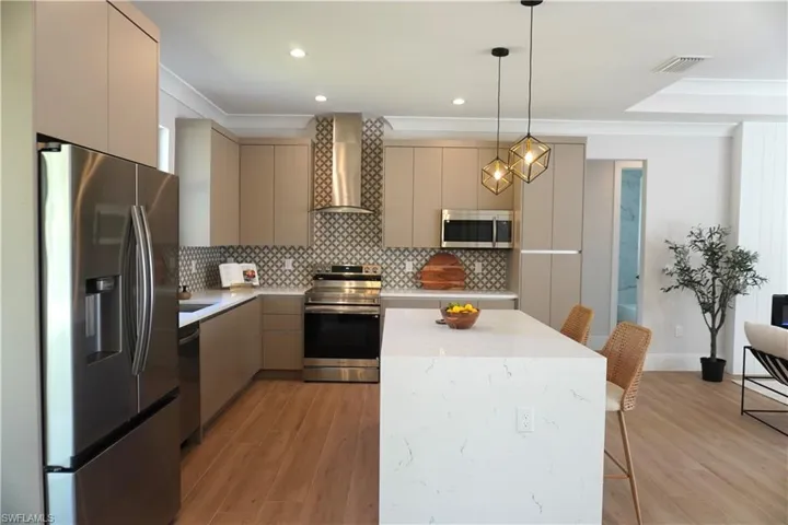 Kitchen featuring flat-panel cabinetry, a quartz-topped waterfall island, stainless steel appliances, a geometric-patterned backsplash, and wood-finish flooring