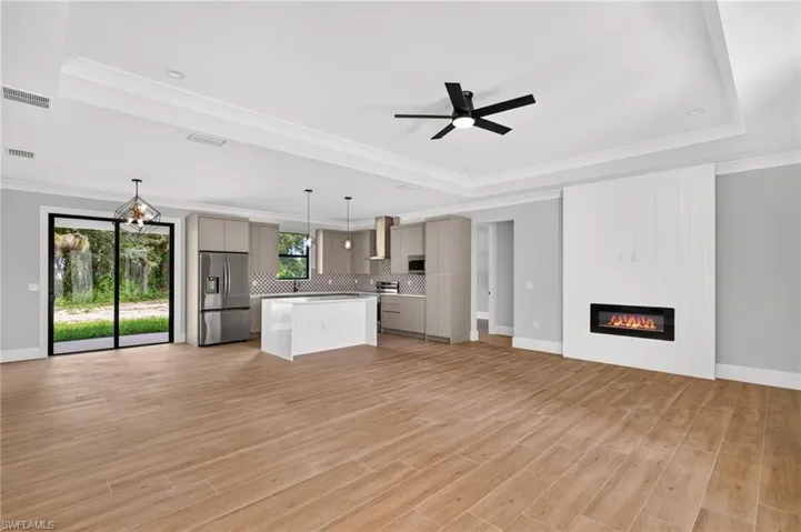 Open-concept living space featuring wood-finish flooring, a contemporary kitchen with stainless steel appliances, a kitchen island with seating, a built-in electric fireplace, and sliding glass doors