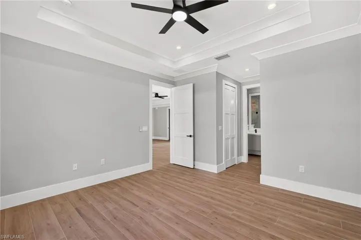 Tray ceiling with recessed lighting and a ceiling fan, wood-finish flooring, and white trim throughout