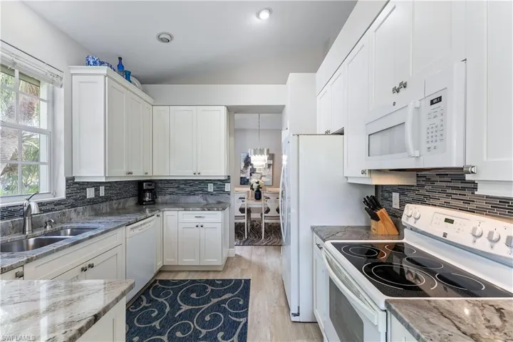 Kitchen featuring white cabinets, light wood-type flooring, white appliances, and backsplash