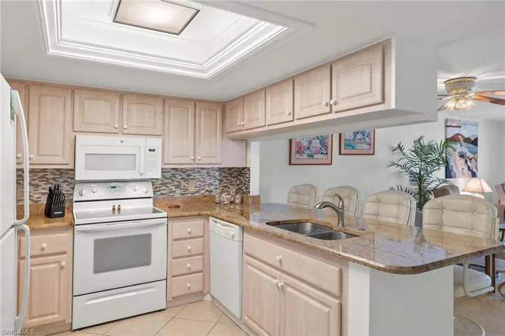 Kitchen with kitchen peninsula, sink, light brown cabinetry, and white appliances