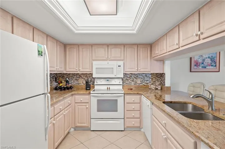 Kitchen featuring light brown cabinets, light stone countertops, sink, and white appliances