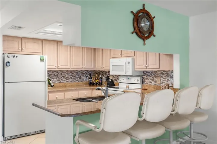 Kitchen with white appliances, sink, kitchen peninsula, and a kitchen breakfast bar