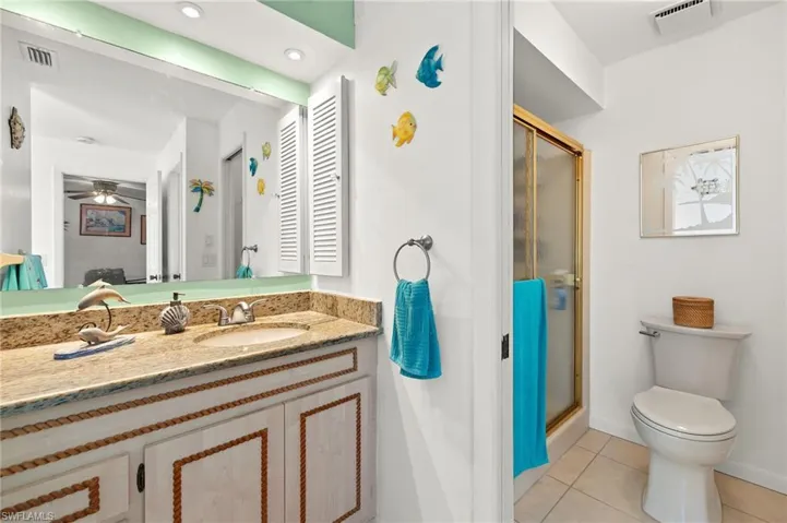 Bathroom with a shower with shower door, toilet, ceiling fan, tile patterned floors, and vanity