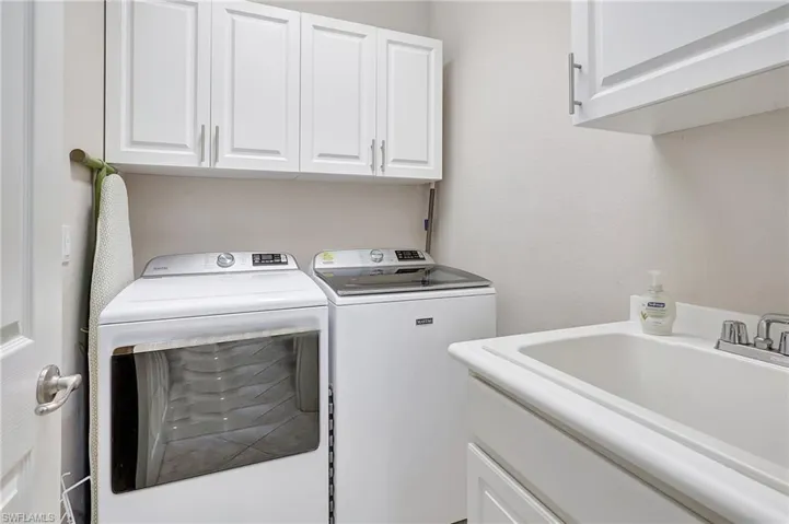 Clothes washing area featuring cabinets, washer and clothes dryer, and sink