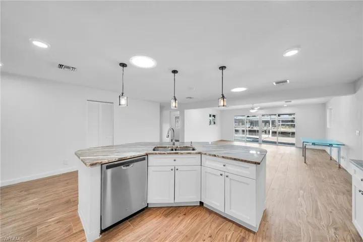 Kitchen with visible vents, dishwasher, light stone countertops, a sink, and light wood-style floors