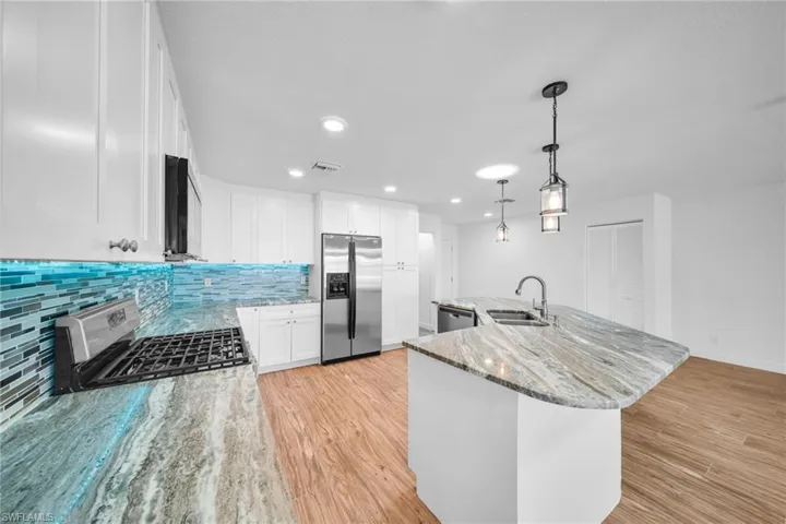 Kitchen featuring backsplash, a sink, light wood-style flooring, stainless steel appliances, and white cabinets