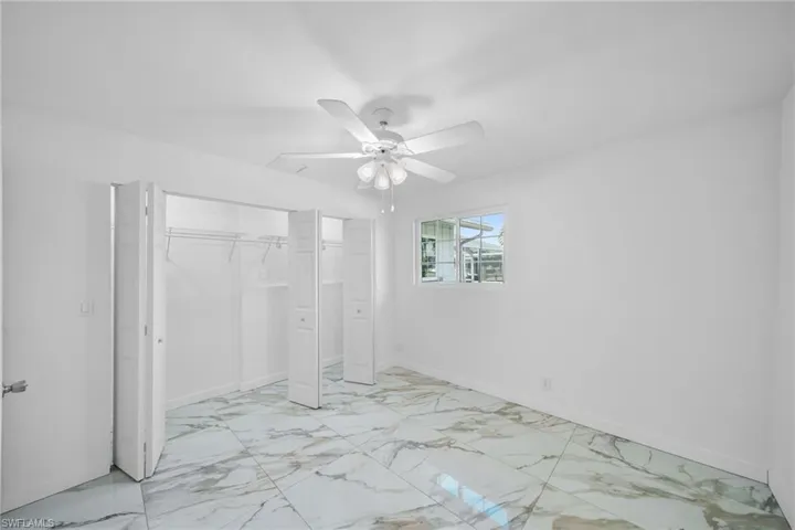 Unfurnished bedroom featuring a closet, marble finish floor, baseboards, and a ceiling fan