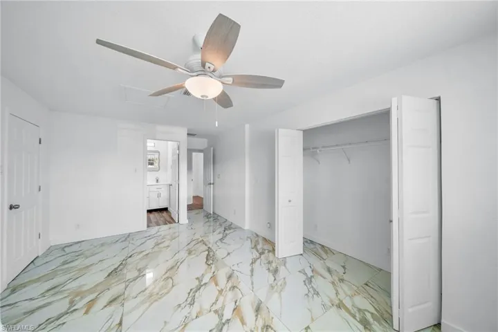 Unfurnished bedroom with a closet, baseboards, marble finish floor, ceiling fan, and connected bathroom