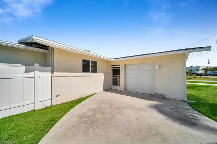 View of side of property featuring driveway, stucco siding, an attached garage, fence, and a lawn