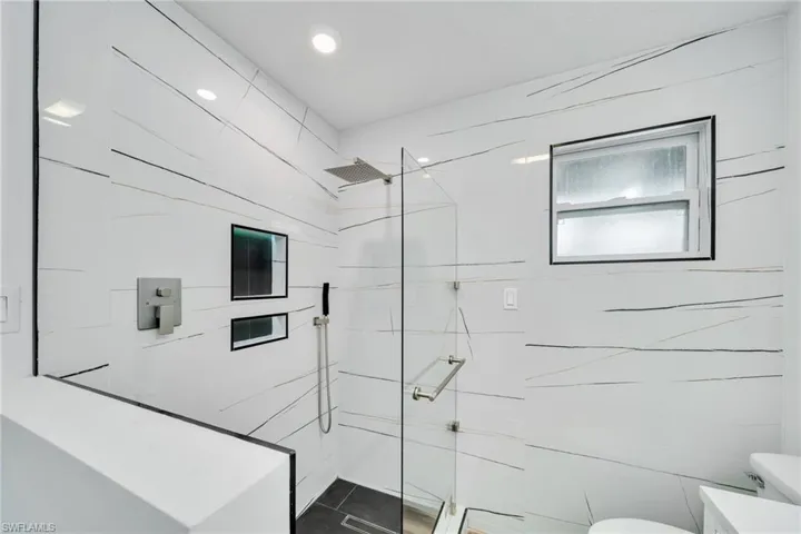 Full bathroom featuring a marble finish shower, toilet, and tile walls