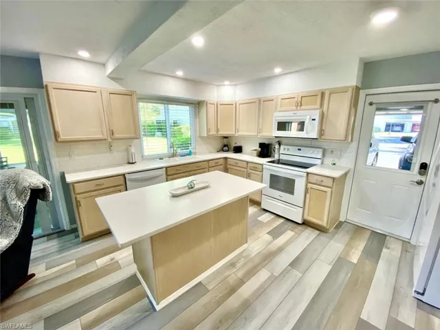 Kitchen featuring light brown cabinetry, white appliances, light countertops, tasteful backsplash, and a center island