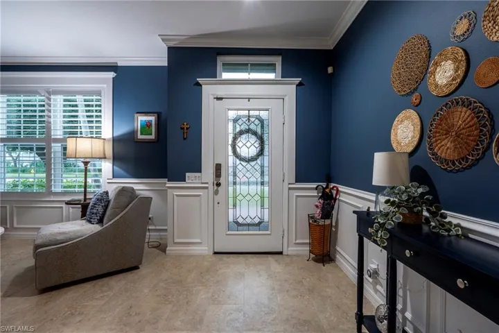 Entrance foyer with ornamental molding, a decorative wall, and wainscoting