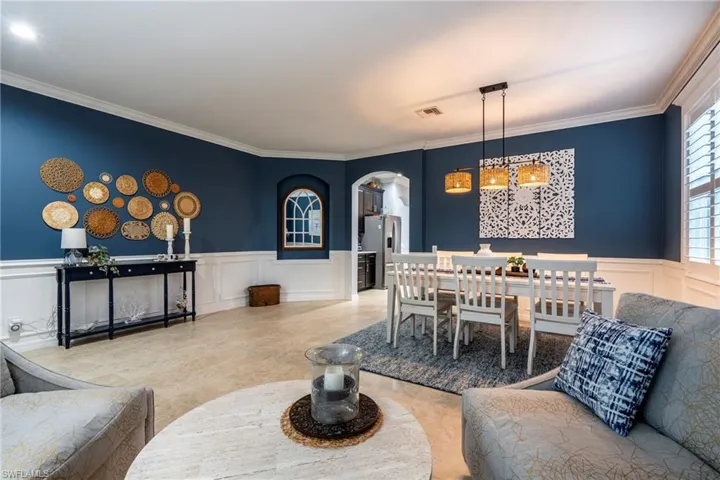 Dining area featuring arched walkways, a decorative wall, wainscoting, and ornamental molding