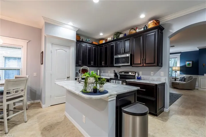Kitchen featuring crown molding, arched walkways, an island with sink, appliances with stainless steel finishes, and dark cabinets