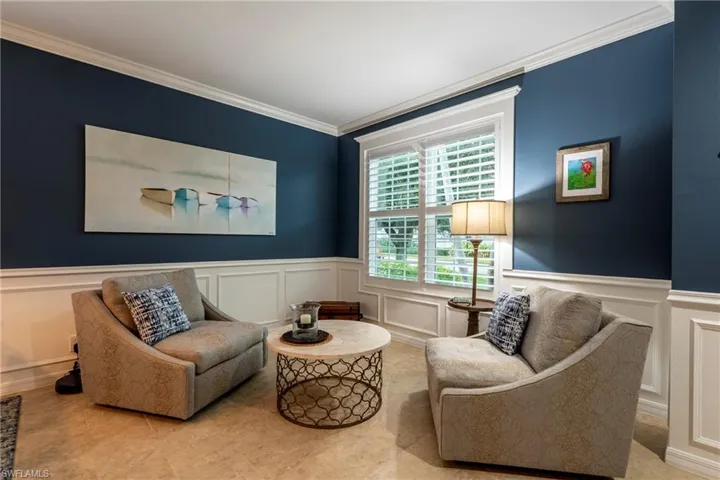 Sitting room with a decorative wall, crown molding, and wainscoting