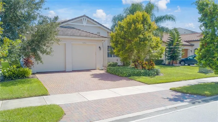 View of front of property featuring decorative driveway, a tiled roof, a front yard, stucco siding, and an attached garage