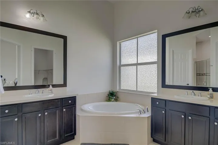 Bathroom featuring a stall shower, two vanities, and a garden tub