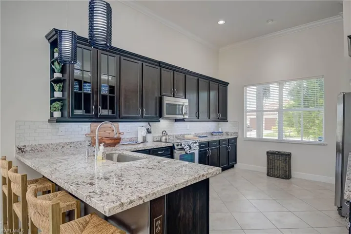 Kitchen featuring light stone countertops, ornamental molding, light tile patterned floors, a peninsula, and tasteful backsplash