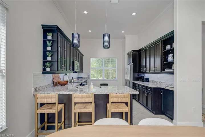 Kitchen with open shelves, backsplash, light stone countertops, crown molding, and a kitchen breakfast bar