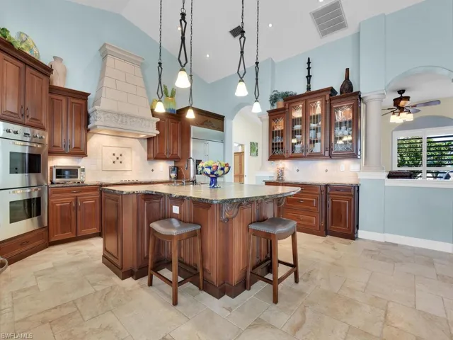 Kitchen featuring custom exhaust hood, a breakfast bar, high vaulted ceiling, pendant lighting, and stainless steel appliances