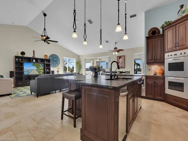 Kitchen with double wall oven, a kitchen island with sink, high vaulted ceiling, sink, and decorative light fixtures