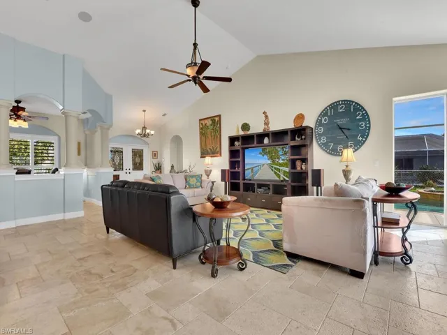 Living room with ornate columns, high vaulted ceiling, and ceiling fan with notable chandelier