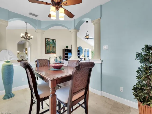 Tiled dining room with ornate columns, lofted ceiling, and ceiling fan with notable chandelier