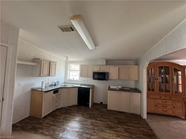 Kitchen with dark wood-type flooring, black appliances, vaulted ceiling, and sink
