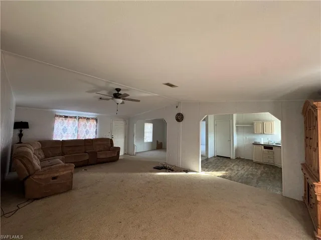 Unfurnished living room with light colored carpet, ceiling fan, and lofted ceiling