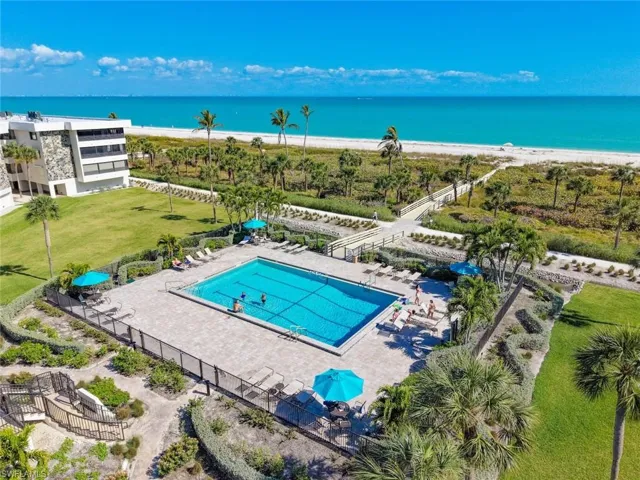 Community pool with a patio, a lawn, and view of water and beach