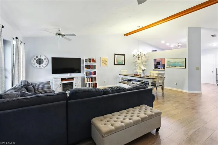 Living room with baseboards, light wood-style floors, vaulted ceiling with beams, and ceiling fan with notable chandelier